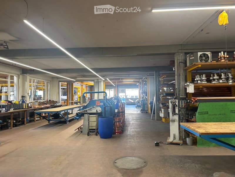 Workshop space with large windows, industrial equipment, tables, shelves, and various tools.