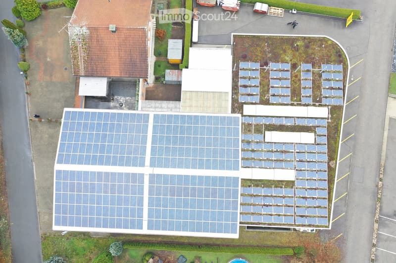 Aerial view of a building with multiple solar panels on the roof, surrounded by a parking lot and greenery.