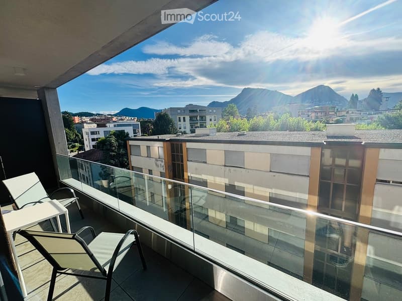 Balcony with glass railing, offering a scenic mountain view, equipped with a table and chairs.