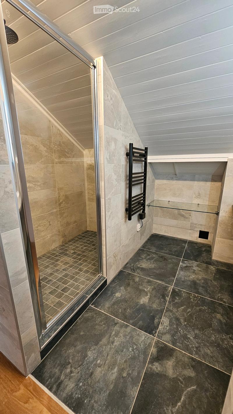 Corner shower, white ceiling, grey tiled floor, glass door, glass shelf, towel rack