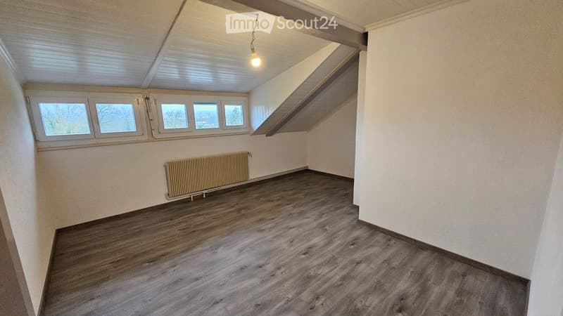 Ample room with wooden floors, white walls, large windows, heating radiator
