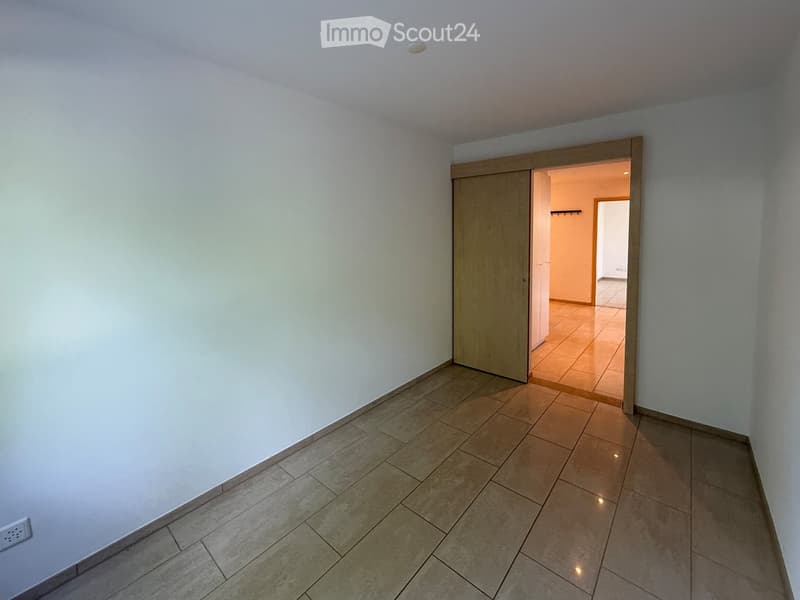 Empty room with tiled floor and white walls, featuring a wooden sliding door leading to another room.