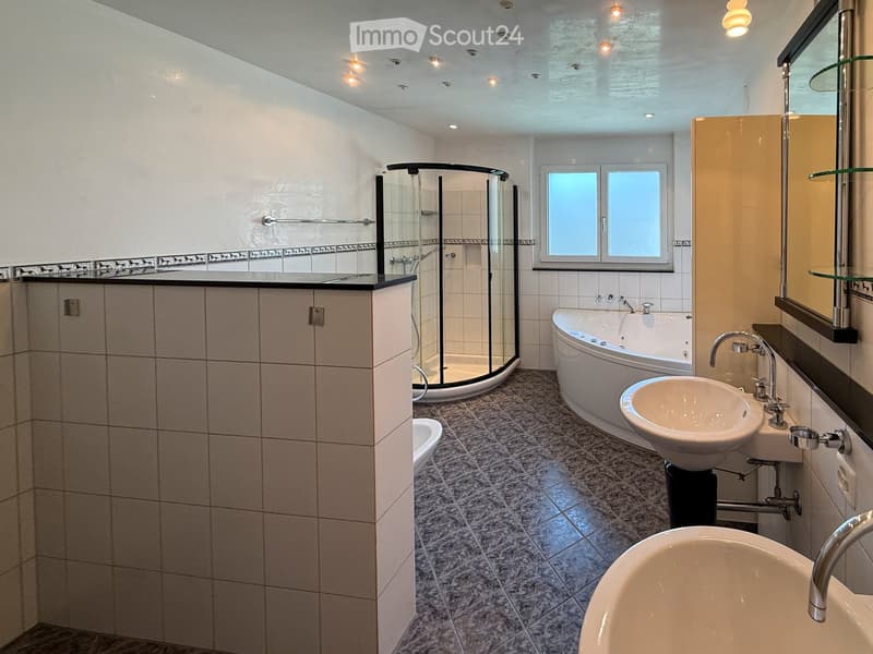 Modern bathroom with a bathtub, sink, mirror, and glass-enclosed shower. Features tiled walls and floor, recessed lighting, and a window for natural light.