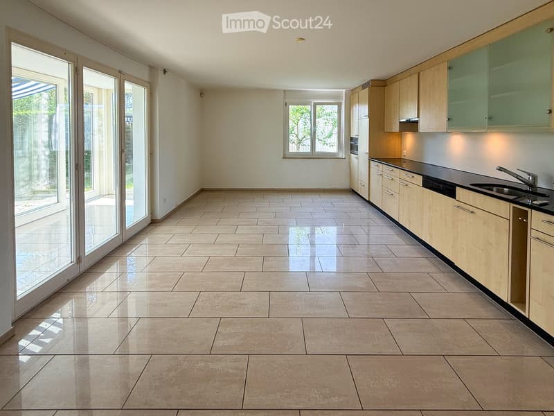 Empty kitchen with light wooden cabinets, black countertops, and large sliding glass doors leading to an outdoor area.