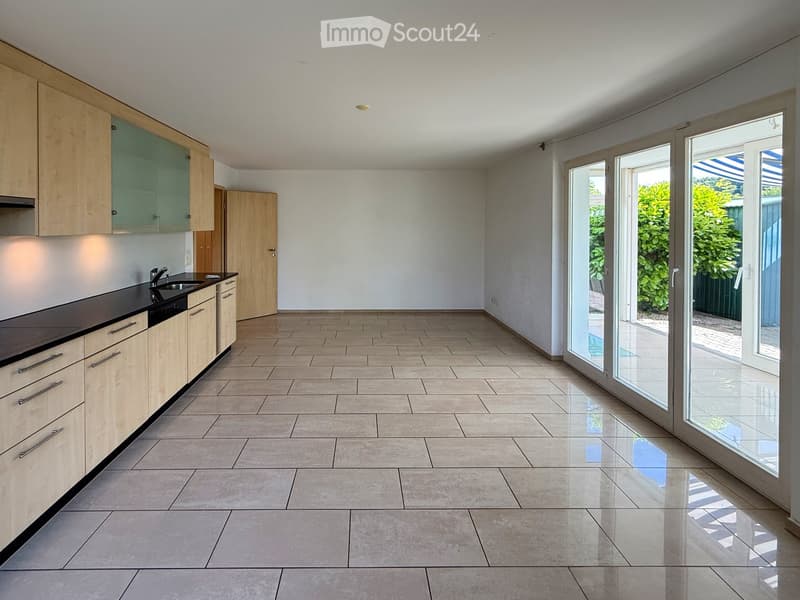 Modern, minimalist kitchen with light wood cabinets, black countertops, and large glass sliding doors leading to an outdoor area.