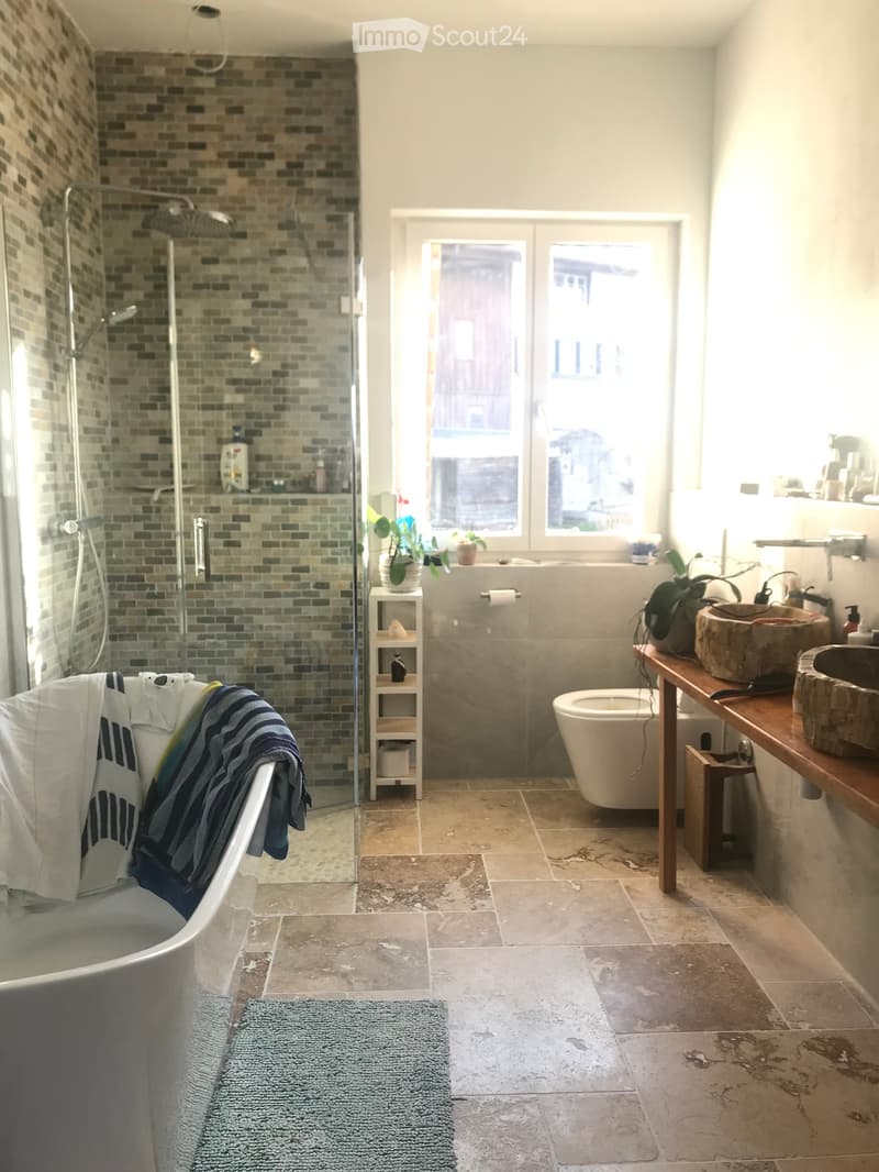 Modern bathroom with a bathtub, toilet, sink, wooden shelf, and a shower area with glass enclosure. The room features tiled walls and a large window with a view.
