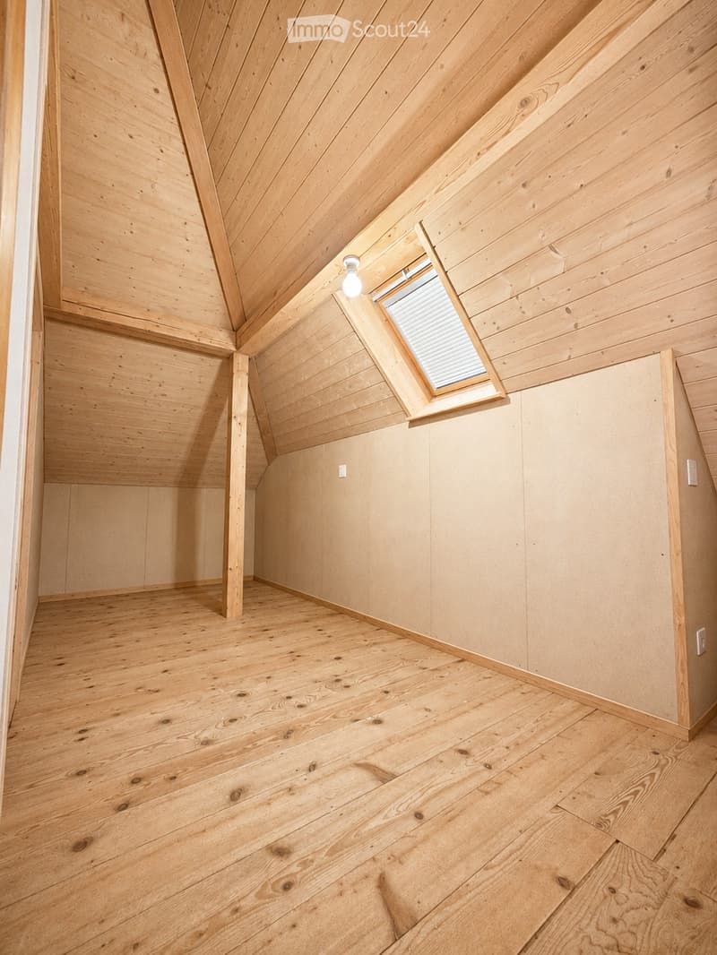 Empty room with wooden walls, ceiling, and floor, featuring a skylight window and exposed wooden beams.