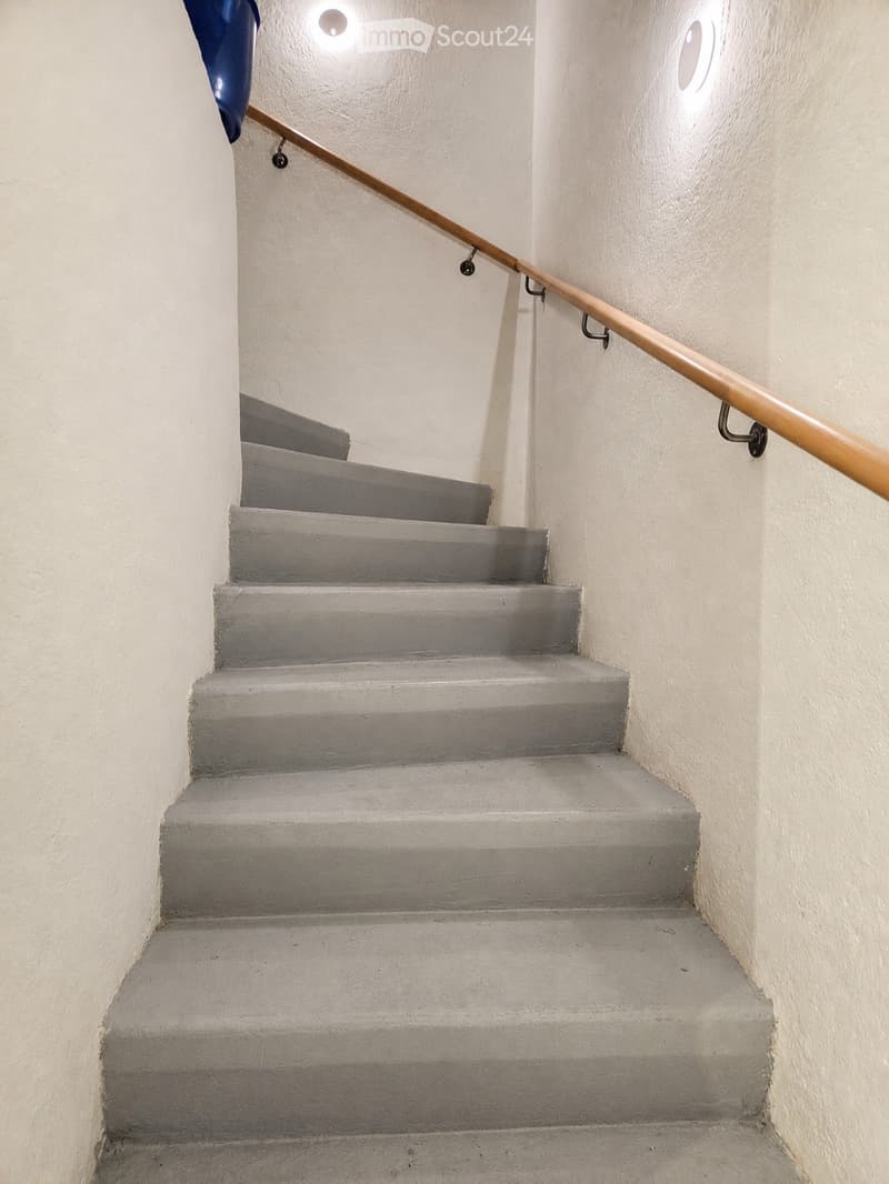 Concrete staircase with wooden handrail and built-in lighting, leading upwards.