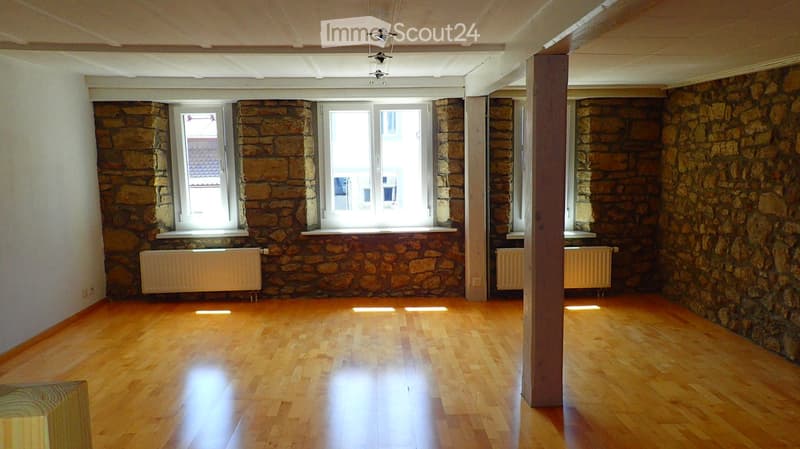 Empty room with wooden flooring, stone walls, and large windows. No furniture or equipment present.
