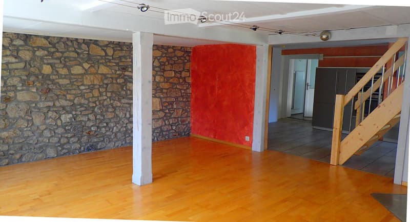 Empty room with wooden flooring, stone walls, and a staircase leading to another area.