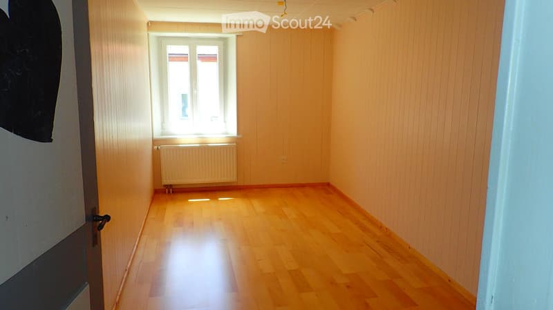 Empty room with wooden flooring, light-colored walls, and a window with a radiator below it.