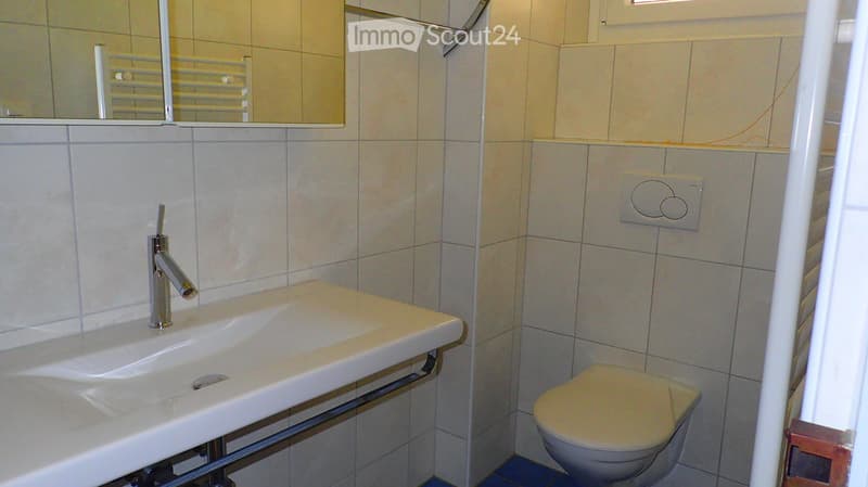 Modern bathroom with a white sink, chrome faucet, toilet, and a mirror above the sink. The walls are tiled in light beige tiles.