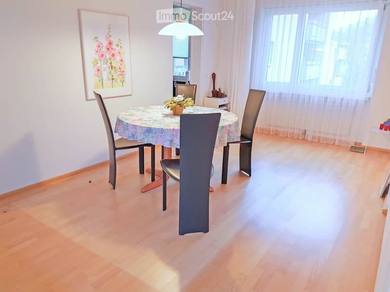 Dining room with a round table, four chairs, a flower vase, a painting, and a window with curtains