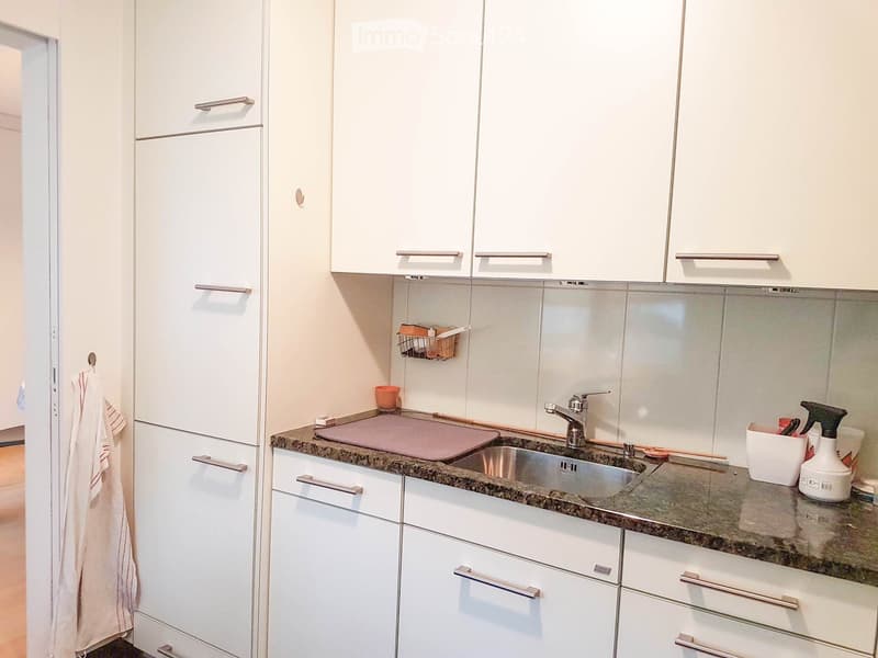 modern kitchen with white cabinets, granite countertop, stainless steel sink, faucet, chopping board, and cleaning products