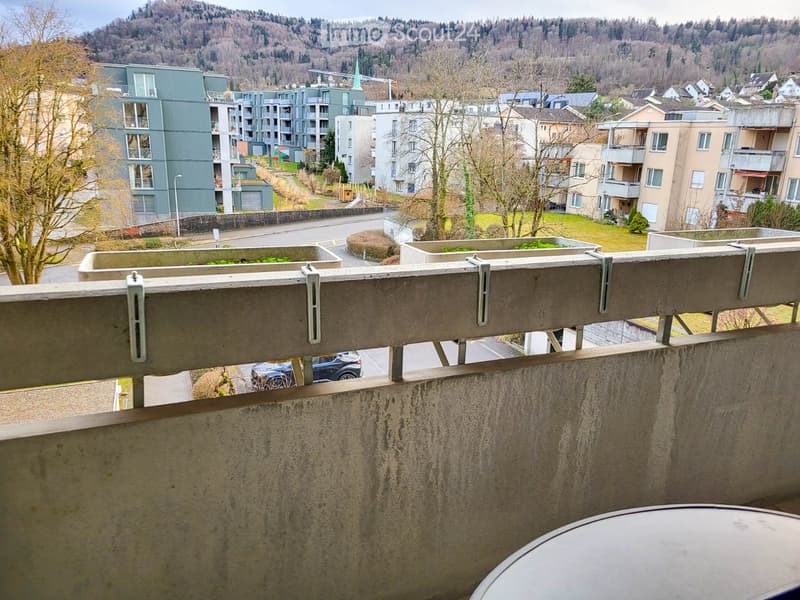 Balcony overlooking a residential area with apartment buildings, trees, and a road below.