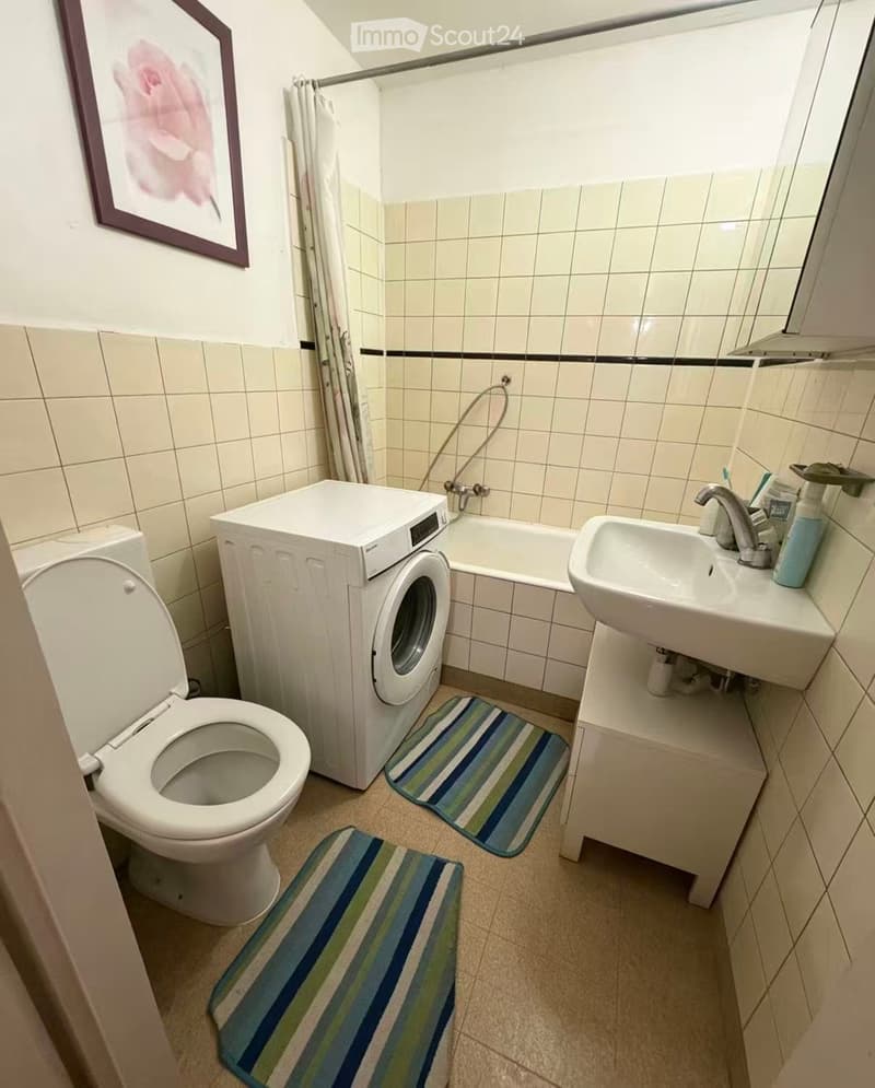 Compact bathroom with a toilet, washing machine, bathtub, sink, and two striped bath mats.