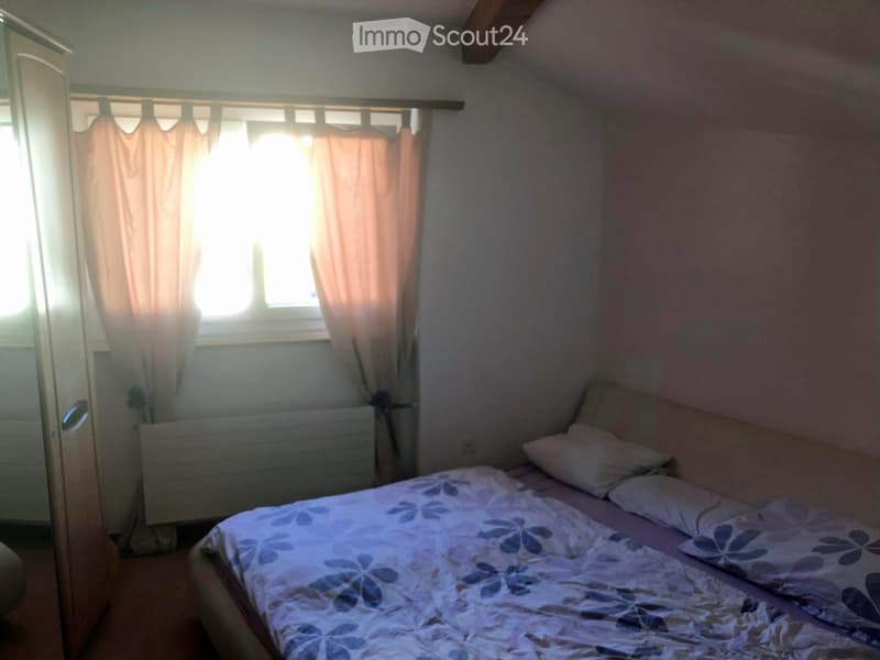 Bedroom with a double bed, pillows, a wardrobe, and a window with curtains.