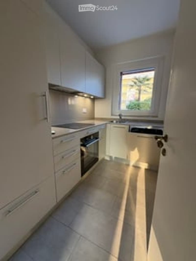 Modern kitchen with white cabinets, a stove, an oven, and a sink, featuring a large window with a view of greenery.