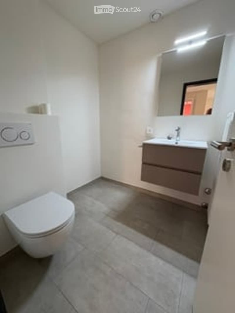 Modern bathroom with white tiled walls, grey tiled floor, white toilet, sink with mirror, and modern lighting.