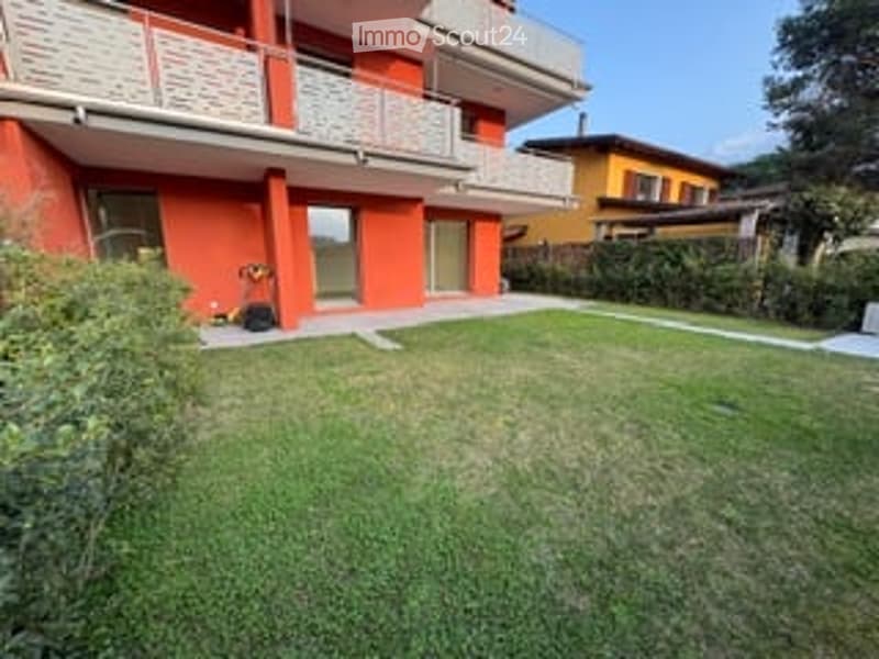 Well-maintained lawn in front of a red apartment building with balconies and large windows.