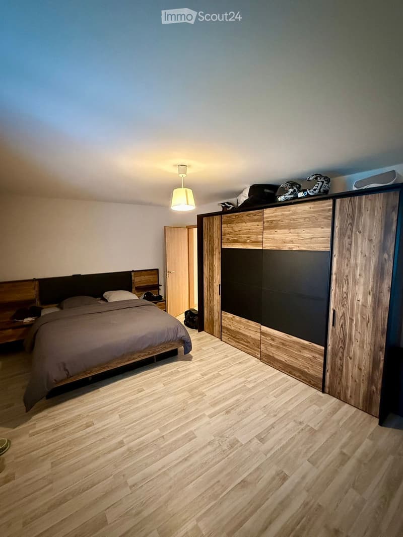 Modern bedroom with wooden flooring, a large bed with dark headboard, a tall wardrobe with wooden and black panels, and a hanging lamp above the bed.