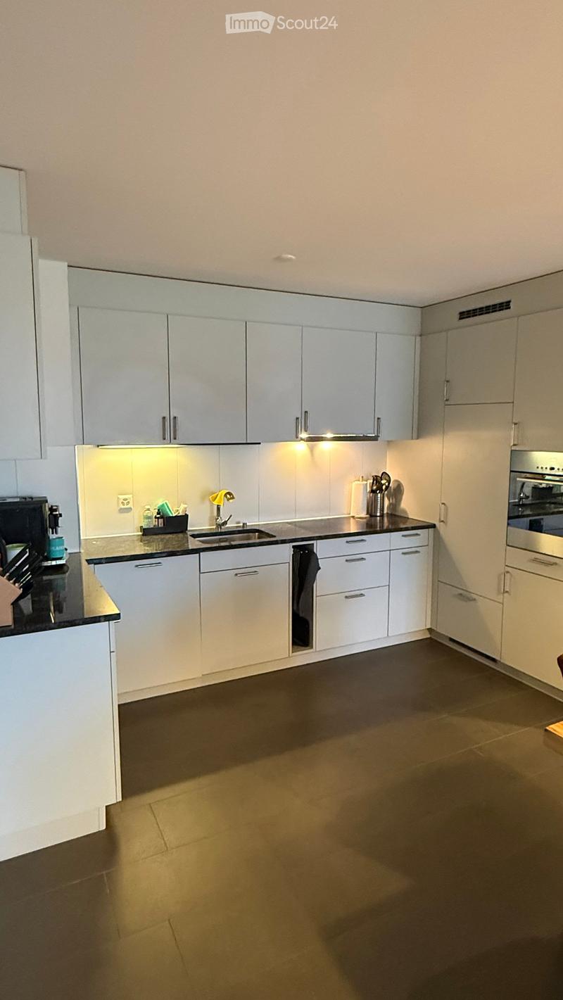 Modern kitchen with white cabinets, dark countertops, and built-in appliances including an oven and coffee maker. Features a sink with a modern faucet, a knife block, and various small items on the counter.