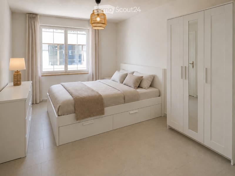 Modern bedroom with a white bed, nightstand, lamp, and large wardrobe. The room features light-colored walls, tiled flooring, and large windows with curtains.