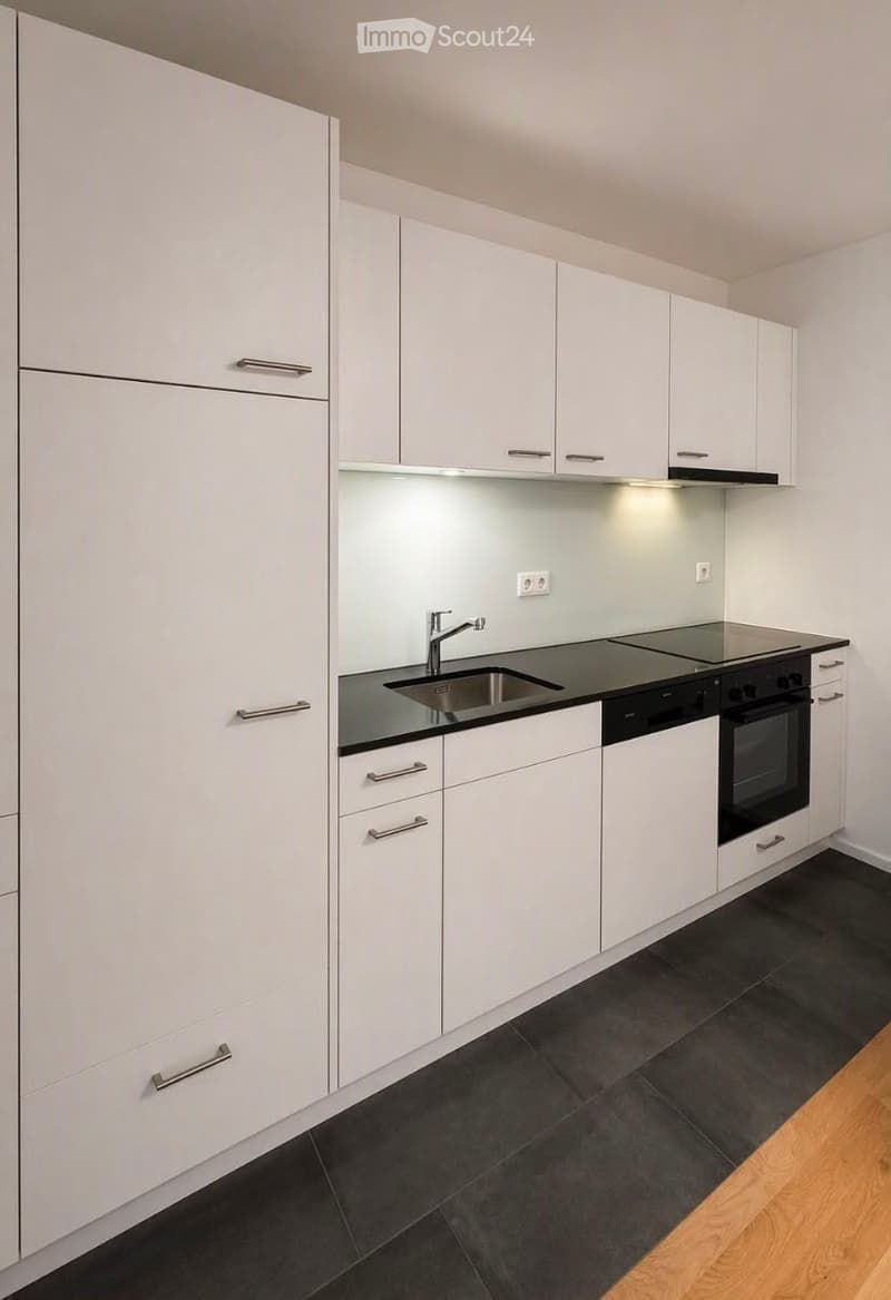 Modern kitchen with white cabinets, black countertops, stainless steel sink and faucet, built-in stove and oven, and dark tiled flooring.