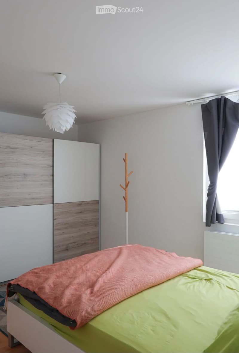 Modern bedroom with a bed, wardrobe, coat rack, and a decorative pendant light.