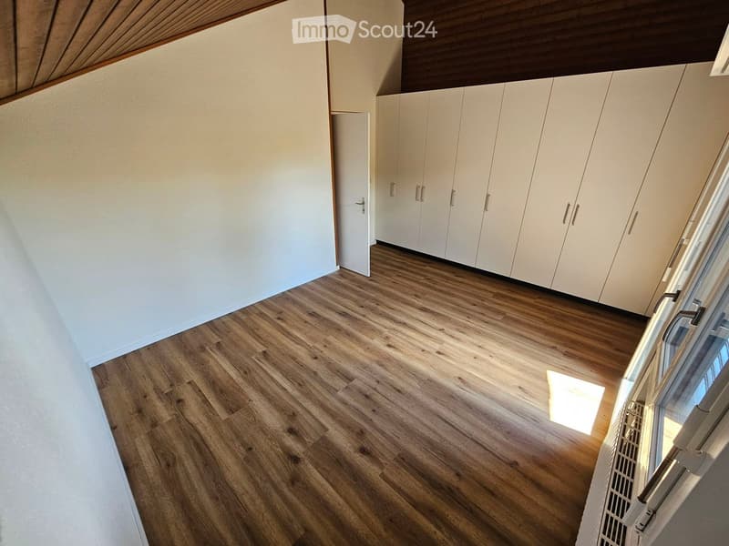 Empty room with light wooden flooring, white walls, built-in white cabinets, and a door leading to another space.