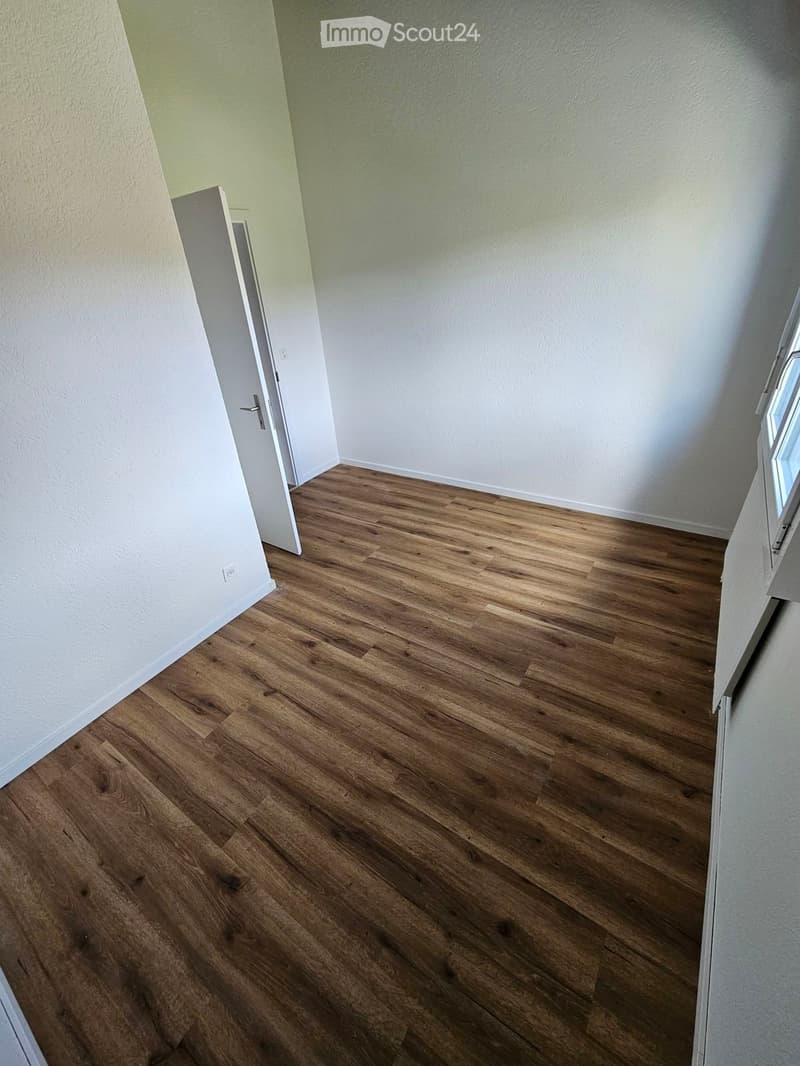 Empty room with wooden flooring and white walls, featuring a door and a window.