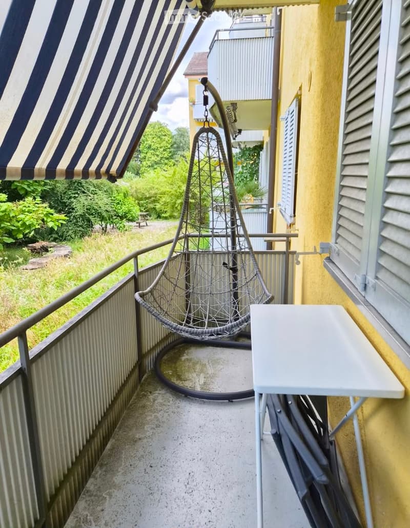 Balcony with a hanging egg chair, a small table, and a view of greenery.