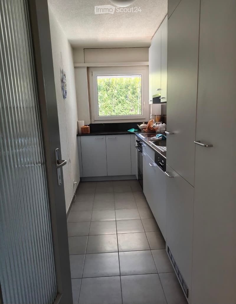 Modern kitchen with white cabinets, tiled floor, and stainless steel appliances. A window provides natural light, and the space is organized with a sink, oven, and dishwasher.