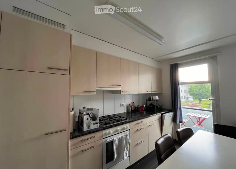 Modern kitchen with light-colored cabinets, stainless steel appliances, and a black countertop. Includes a refrigerator, oven, stove, dishwasher, toaster, coffee maker, and a small dining area with a table and chairs.