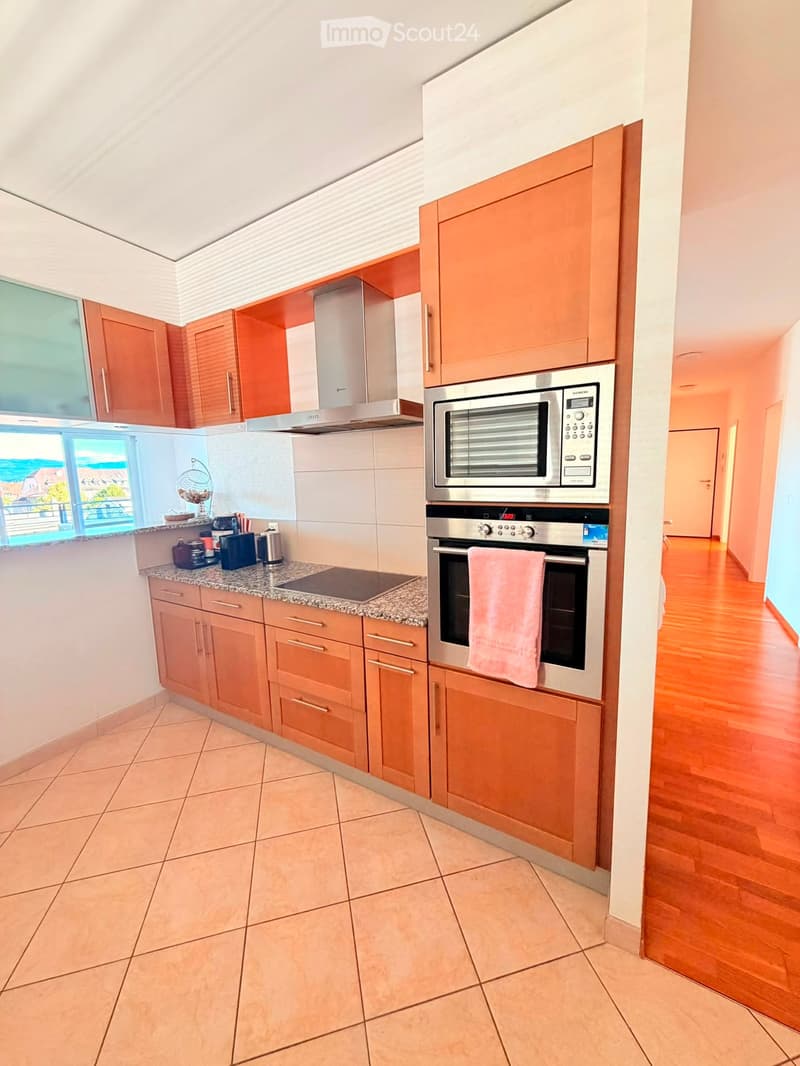 Modern kitchen with light wooden cabinets, stainless steel appliances, granite countertop, and a view of the balcony.