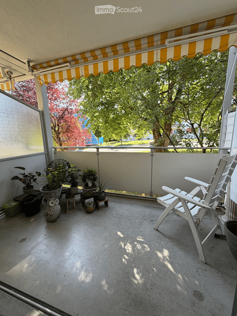 Balcony with striped awning, potted plants, and white plastic chair.