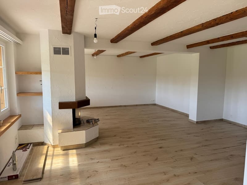 Empty room with wooden floors, white walls, exposed wooden beams, and a fireplace. There are no furnishings or decorations present.