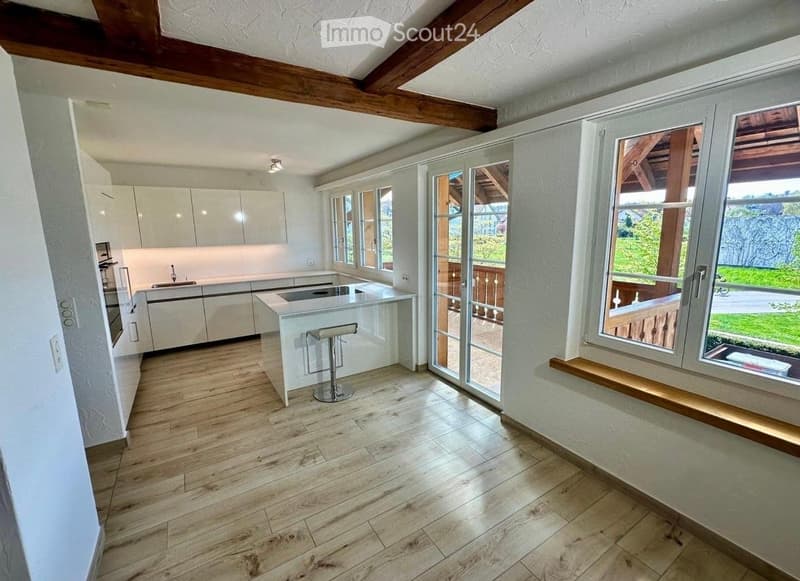 Modern kitchen with white cabinetry, wooden flooring, island with bar stool, and large windows opening to a balcony.