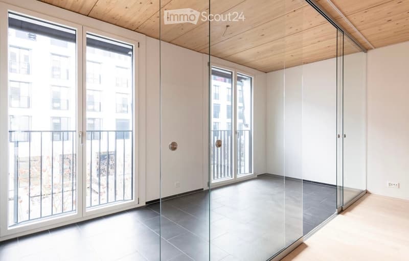 Empty room with large glass doors leading to a balcony, light wooden ceiling, and modern flooring.