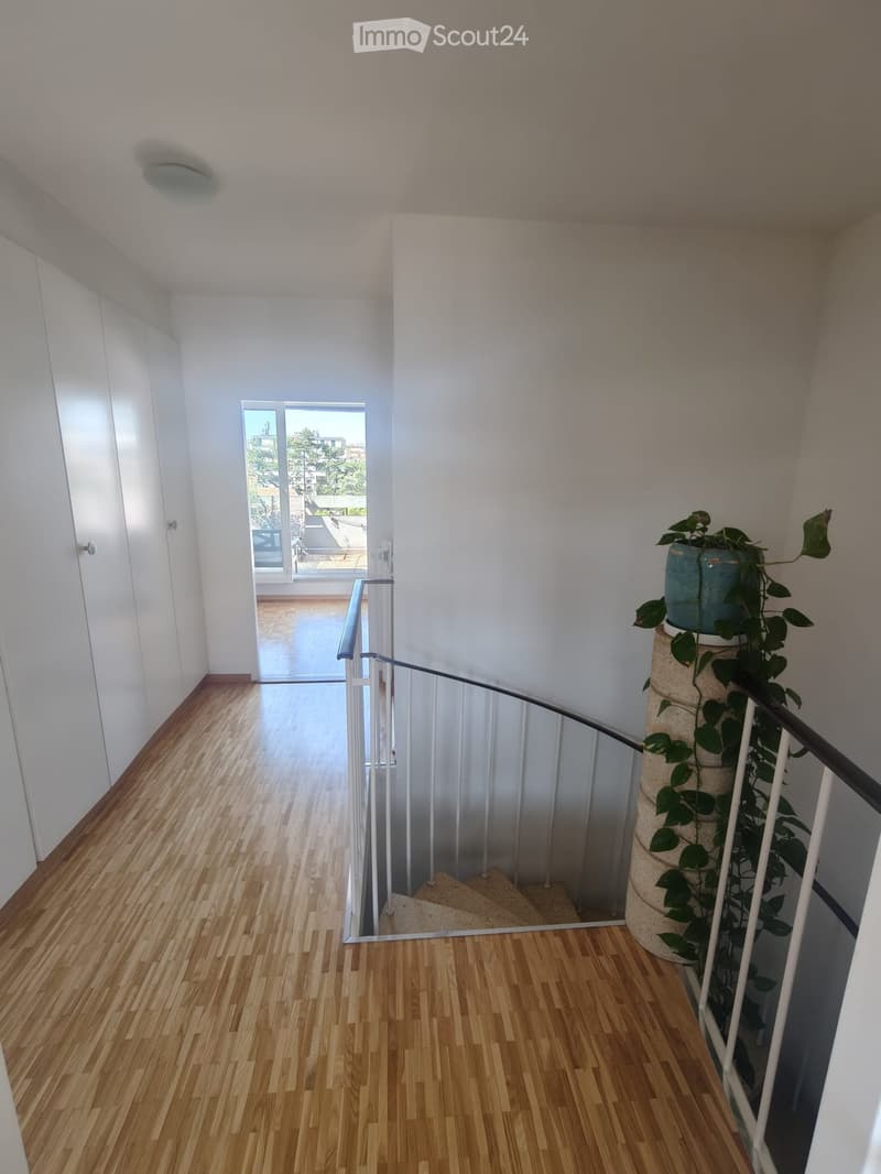 Modern hallway with wooden flooring, white walls, and a staircase leading to a balcony area with outdoor view.