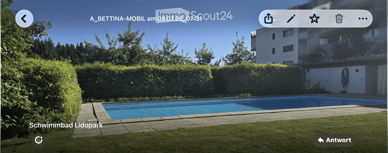 Outdoor area with a swimming pool, surrounded by neatly trimmed hedges and a well-maintained lawn, with a multi-story building in the background.