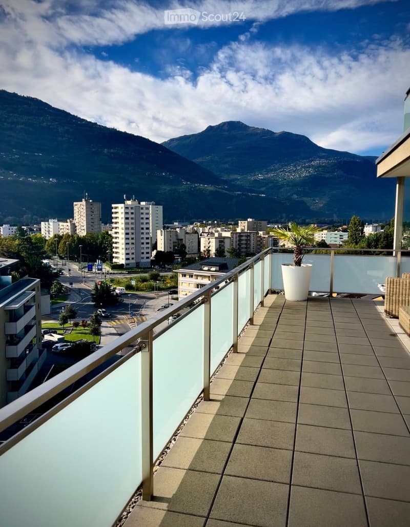 Balcony with tiled floor, glass railing, and a view of the city and mountains.
