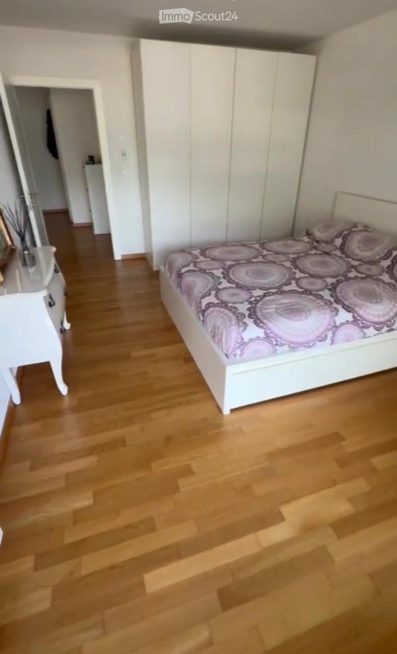 Modern bedroom with wooden flooring, white wardrobe, bed with patterned bedding, and a nightstand with a decorative item.