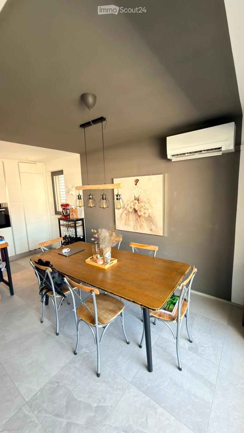 Dining area with a wooden table, six chairs, a laptop, a cup, a vase with dried flowers, a picture frame, a wine rack, an oven, and an air conditioner.