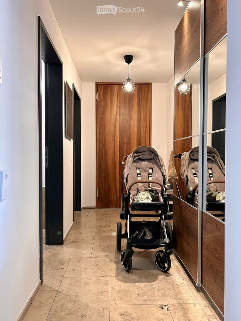 Modern hallway with tiled floor, wooden doors, pendant lights, and a stroller placed in the center.