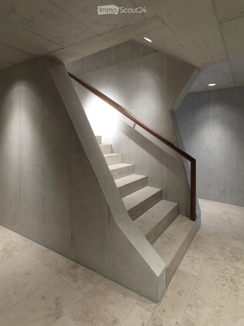 Modern concrete staircase with sleek design, featuring a wooden handrail and recessed lighting.