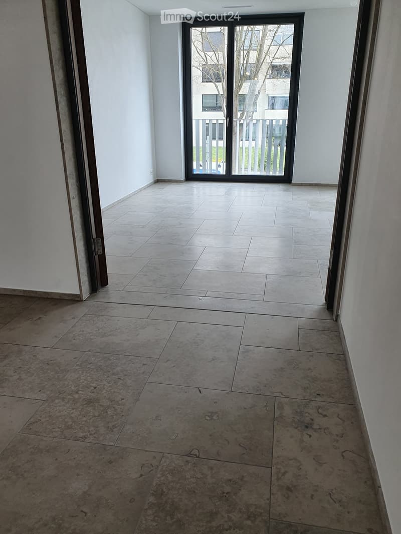 Empty hallway with tiled floors and white walls, featuring a large sliding glass door leading to an outdoor area.