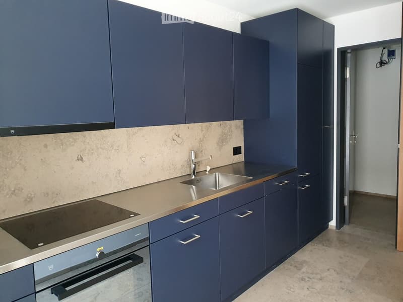 Modern kitchen with dark blue cabinets, stainless steel sink, faucet, and built-in stove and oven. Beige backsplash and countertop.