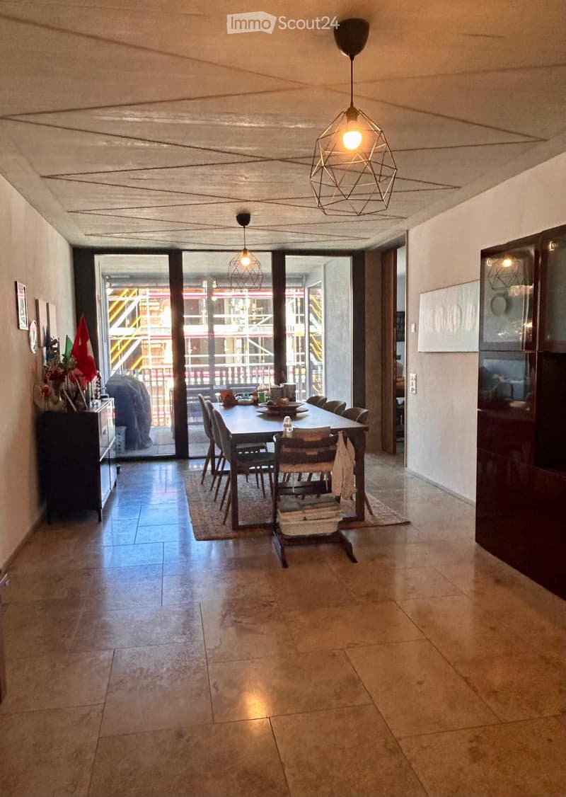 Dining area with a wooden dining table, chairs, a cabinet, and a view of a balcony through large glass doors.