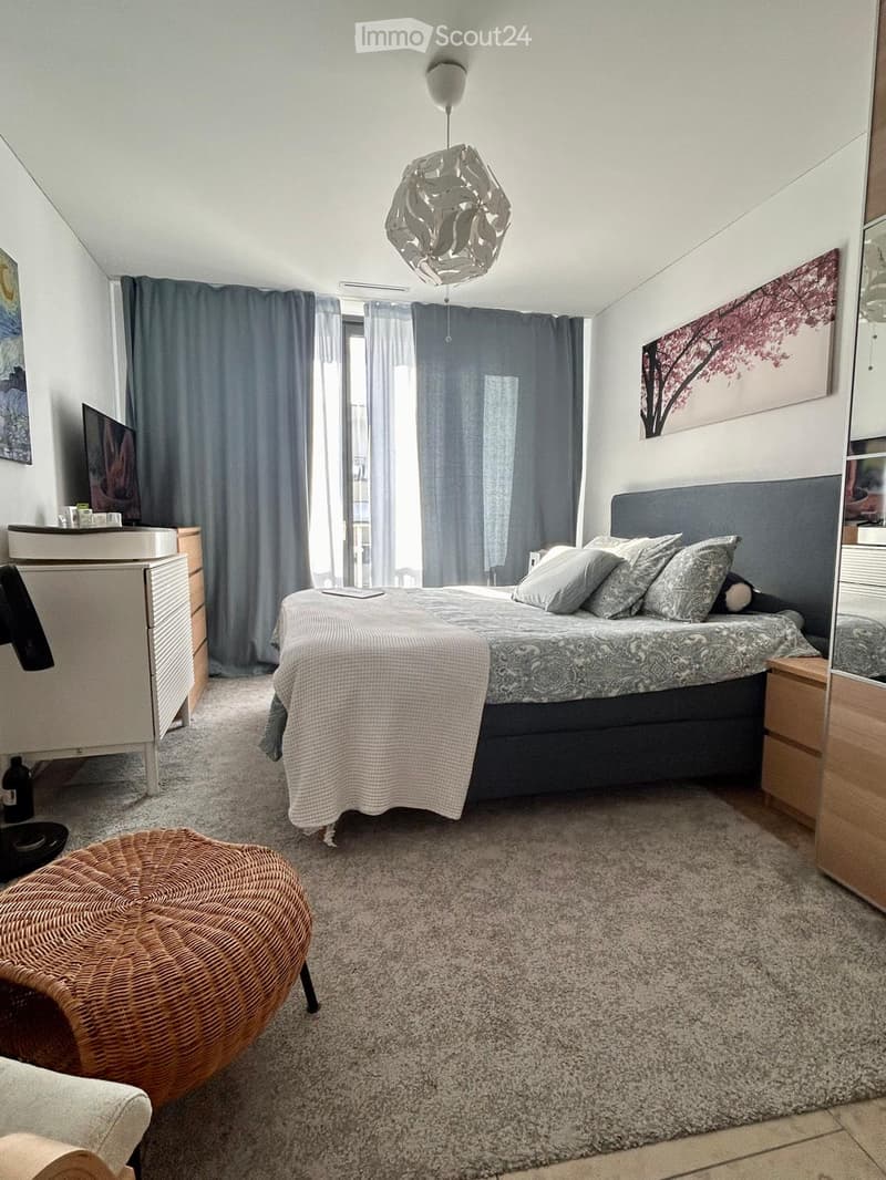 Modern bedroom with a large bed, nightstands, a round wicker stool, a mirror, a screen, and a painting on the wall.